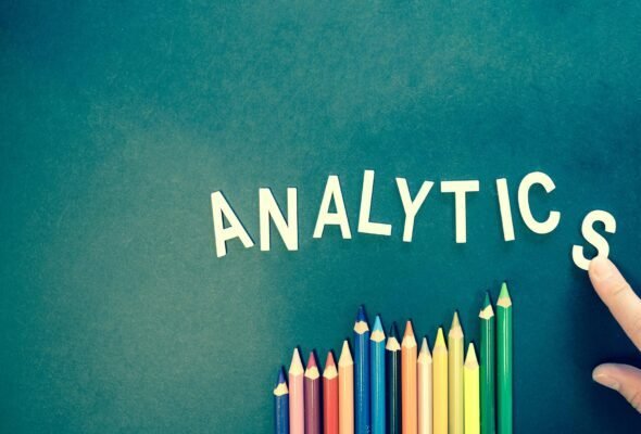 Colored pencils and letters spelling 'ANALYTICS' on a textured background with a hand.