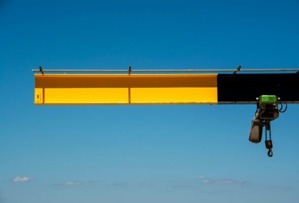 Bright yellow crane arm extending against a clear blue sky, ideal for industrial themes.