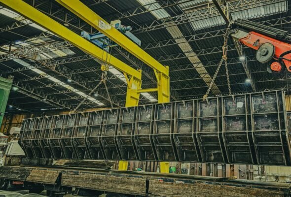 A robust industrial crane hoists a large metal container inside a spacious warehouse setting.